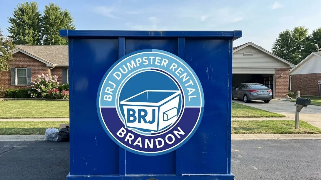 Residential dumpster rental in Brandon: a 20 yard roll-off set on plywood across a flat concrete driveway off Lumsden Road, garage door up and 1970s cabinets, carpet and lanai screen frame stacked flat across the floor of the container. Residential dumpster rental in Brandon: a 20 yard roll-off set on plywood across a flat concrete driveway off Lumsden Road, garage door up and 1970s cabinets, carpet and lanai screen frame stacked flat across the floor of the container.